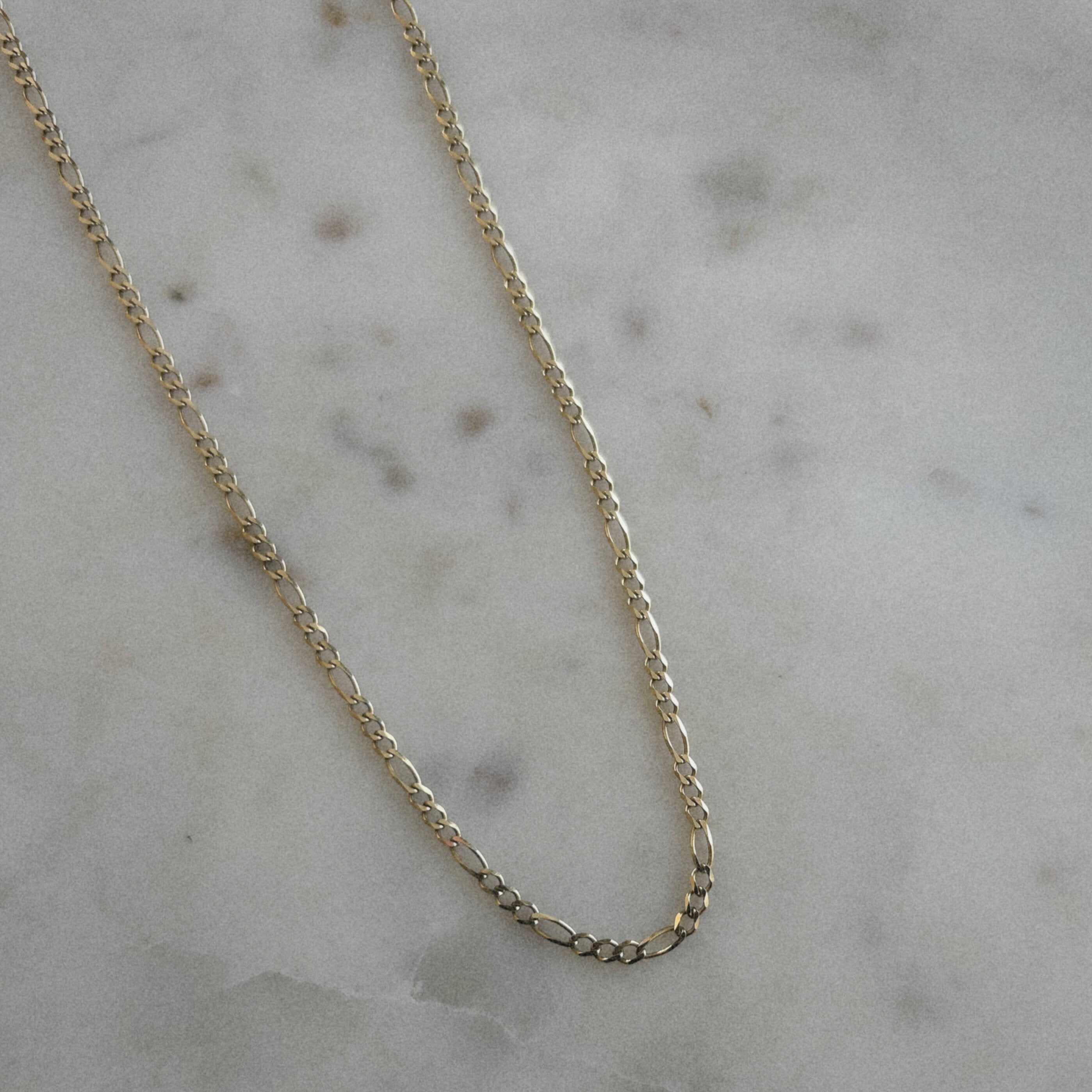 image of a gold figaro chain on a marble table