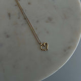 image of a 14k heart pendant with a triple gold color singapore chain against a marble backdrop