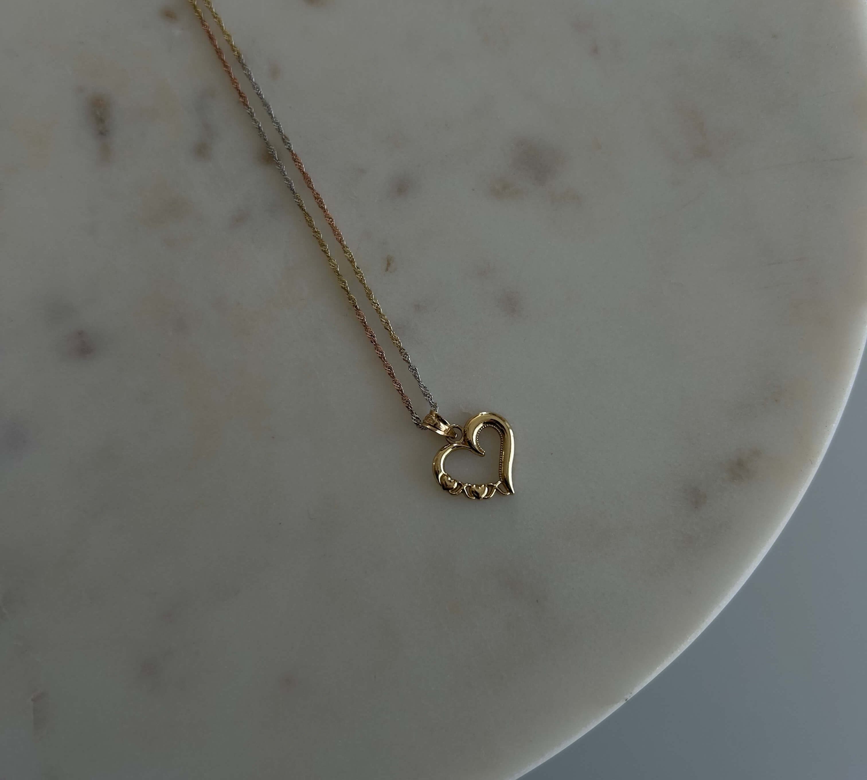 image of a 14k heart pendant with a triple gold color singapore chain against a marble backdrop