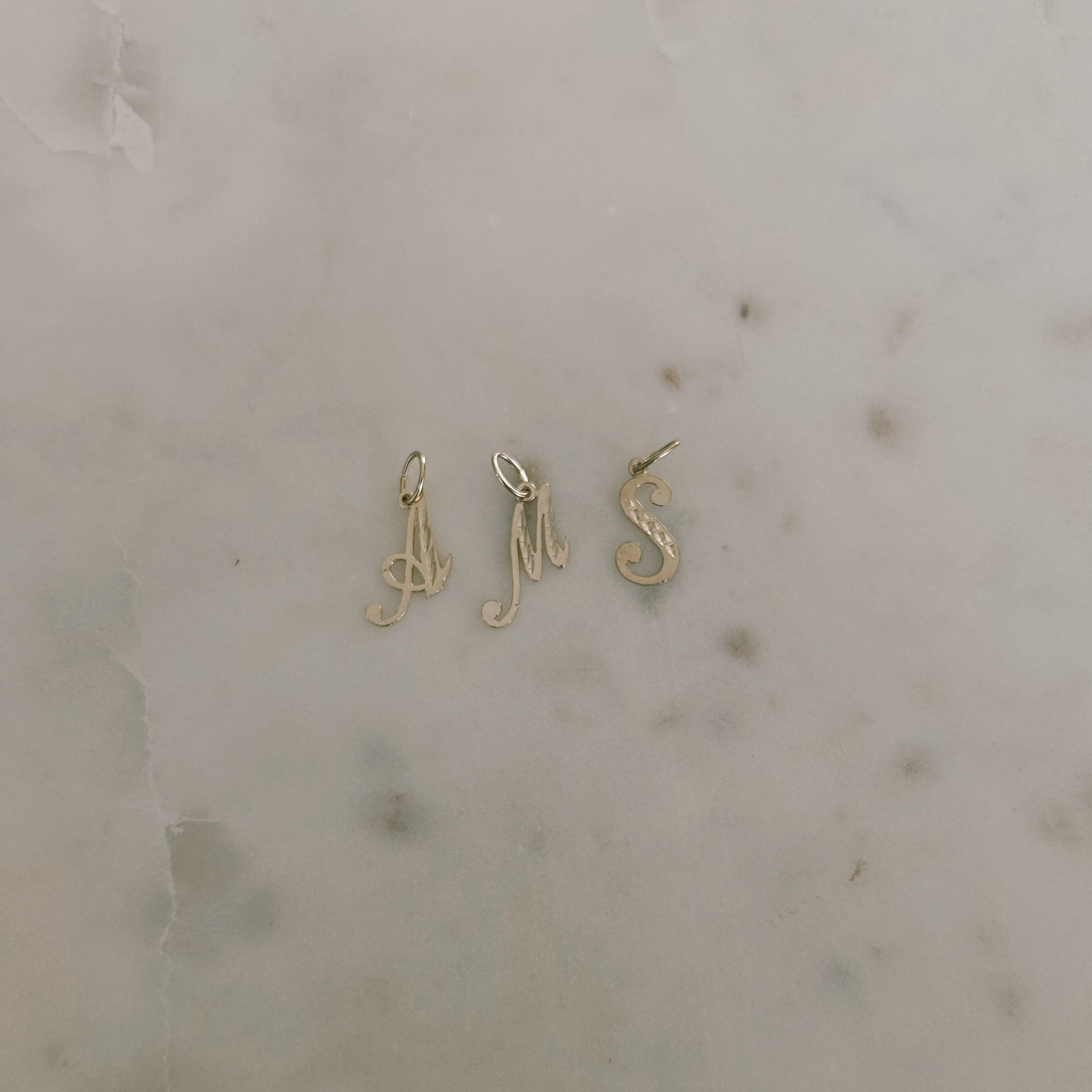 image of gold letter pendants a, m and s against a marble backdrop