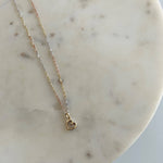 image of a two tone heart pendant with a three tone singapore chain against a white marble block