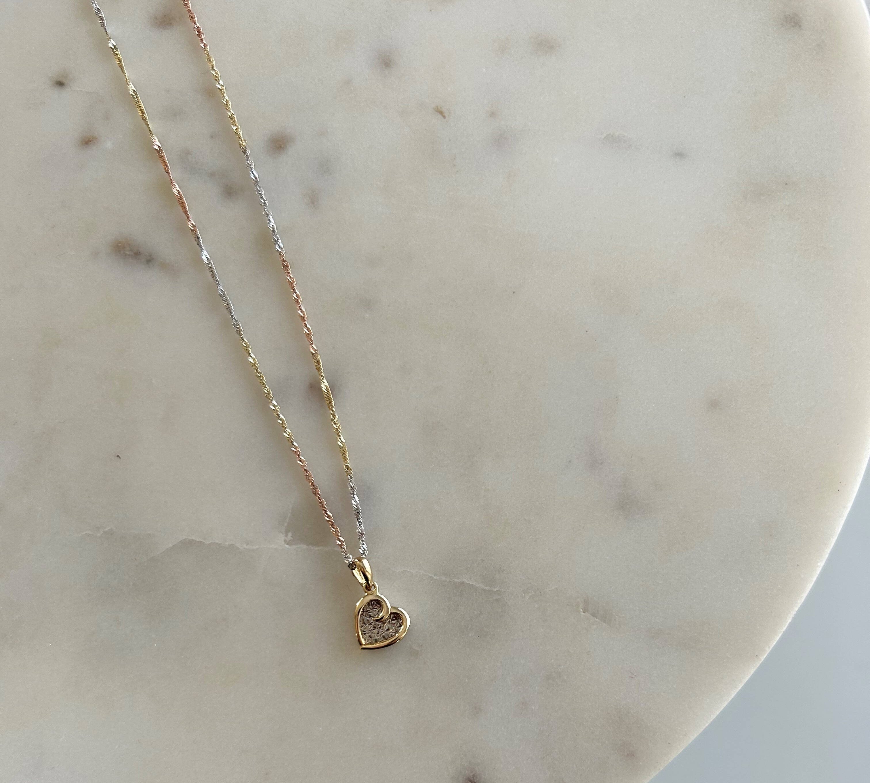 image of a two tone heart pendant with a three tone singapore chain against a white marble block